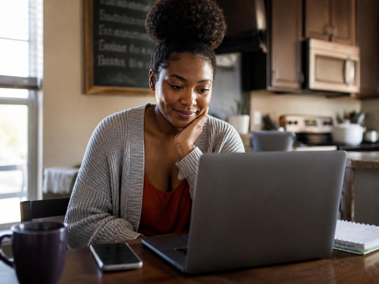 An adult student at her kitchen table exploring career options on a laptop